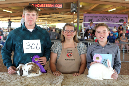 BEST OF SHOW BREEDERS - JD Runyan, left, of the Artesia FFA and Kelby Shook, right, of Cottonwood 4-H, display their Best of Show and Best Opposite breeder rabbits Tuesday morning alongside rabbit show judge Mary Jo Terry of Cameron, Texas. (Elizabeth Lewis - Daily Press)