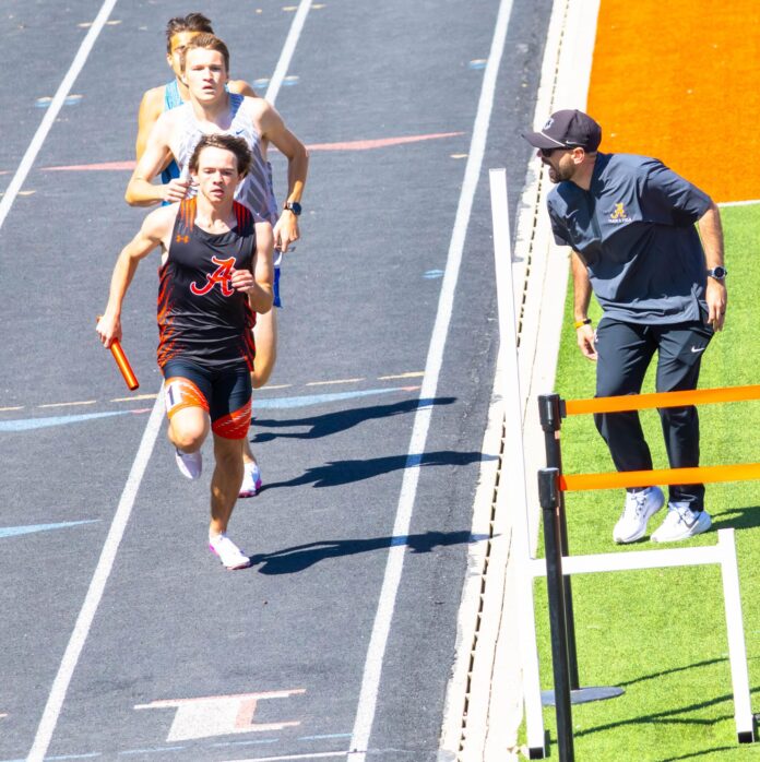 Artesia’s AJ Garcia runs with encouragement from assistant track coach Nicholas Rivera during a meet at the Bulldog Bowl.